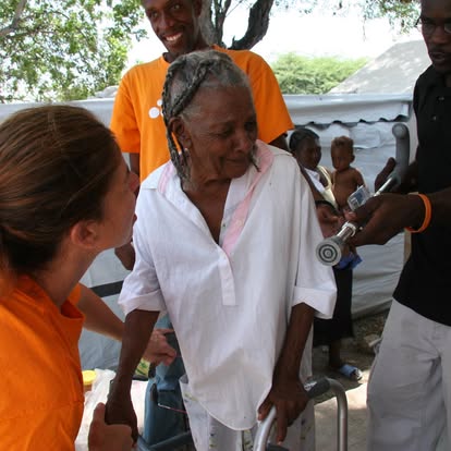 Two people in orange shirts help a woman who was just given a walker