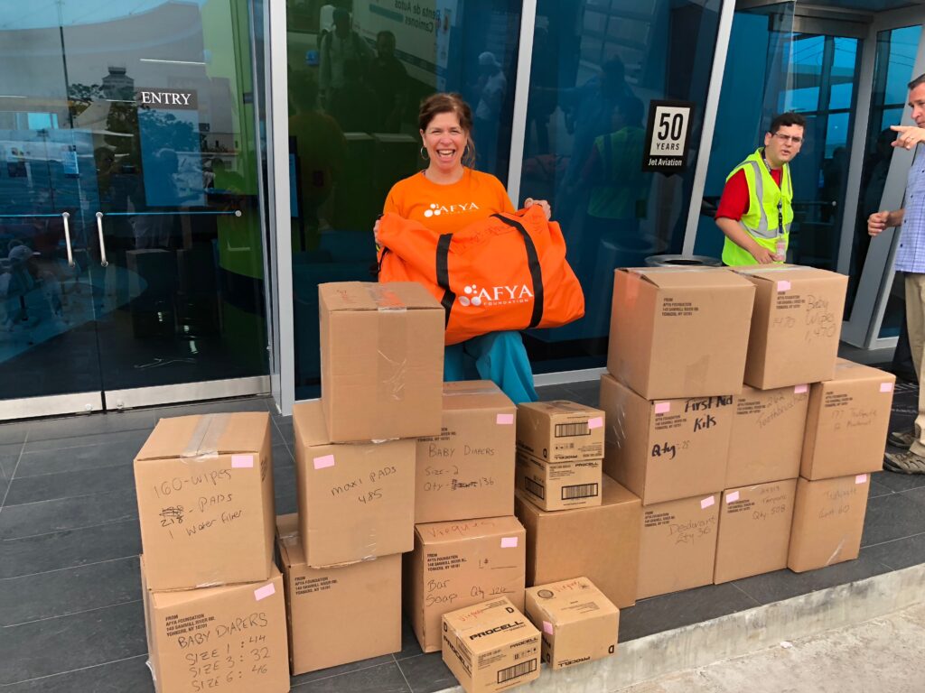 Danielle Butin stands behind a bunch of boxes as she holds an Afya duffel bag and looks excited.