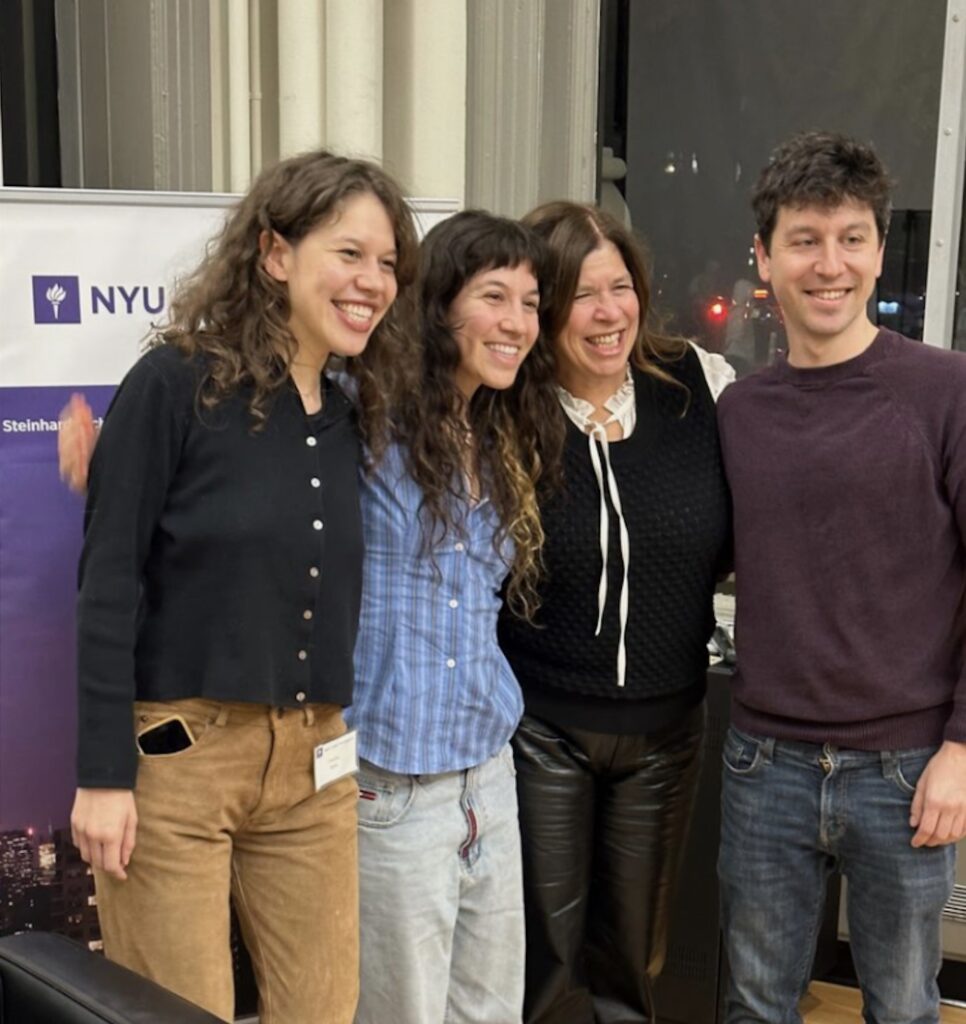Two daughters, Danielle Butin and her son Sam stand smiling for a photo in front of an NYU banner